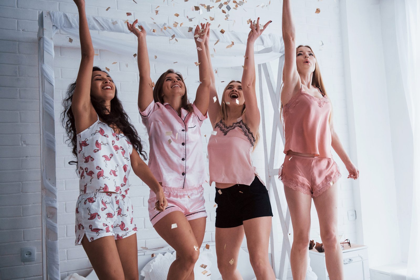 levanta las manos lo mas alto posible confeti en el aire las chicas jovenes se divierten en la cama blanca en una bonita habitacion scaled